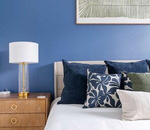 Un dormitorio con cama, mesita de noche con lámpara y una obra de arte en la pared.