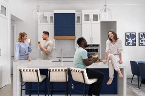 Cocina moderna con armarios blancos, una isla central con taburetes y lámparas colgantes.