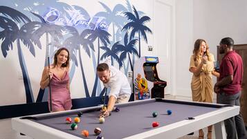 A pool table with balls, a neon sign, and a mural of palm trees.