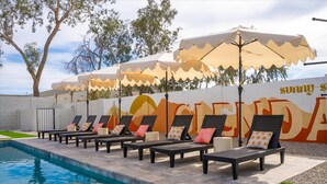 A poolside area with lounge chairs and umbrellas, a mural with the word 'SUNNY' on the wall, and a clear blue pool. - The Lazy Palm Private Lazy River Pickleball (Glendale)