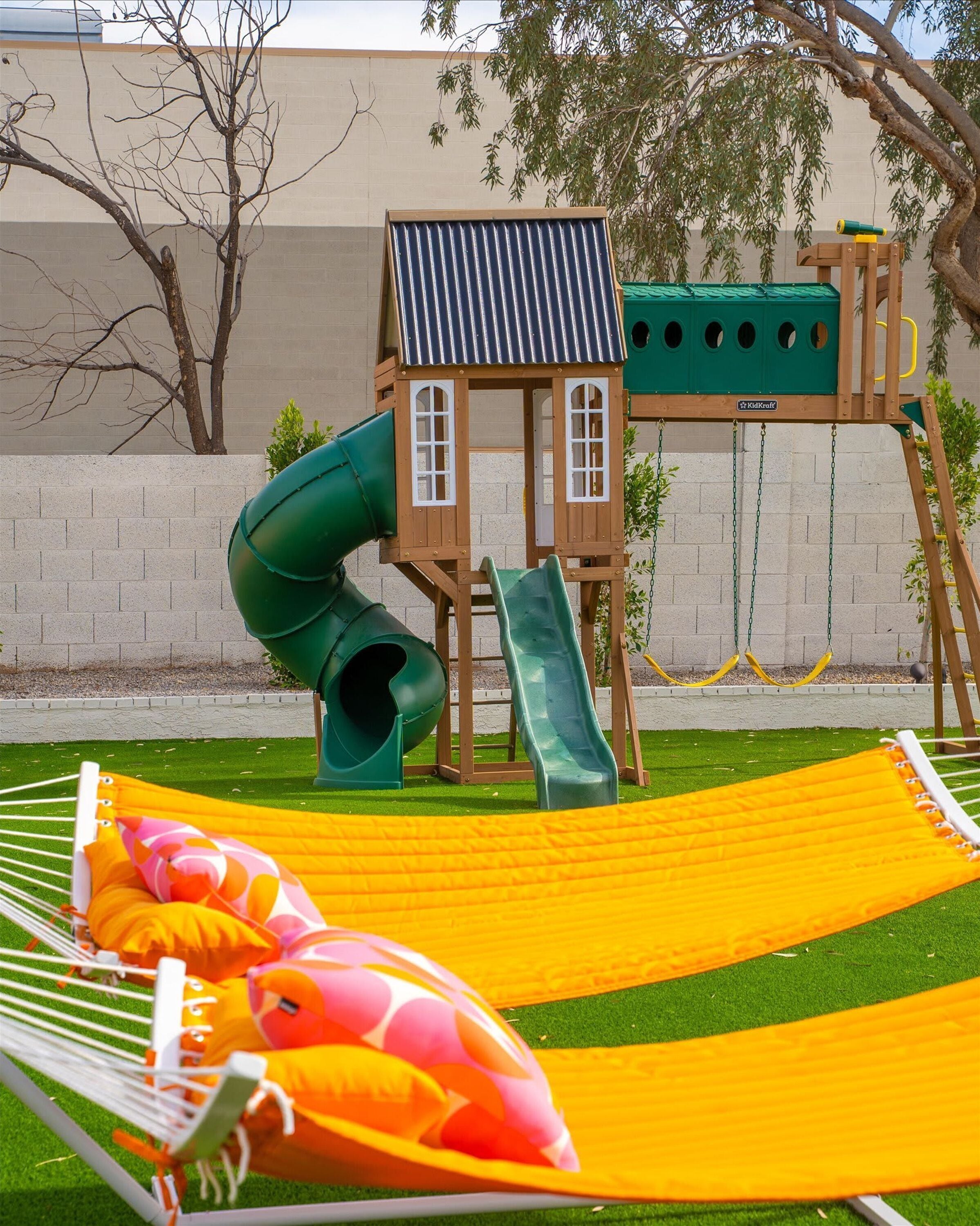 A playground with a slide and swings, a hammock, and a green playhouse.