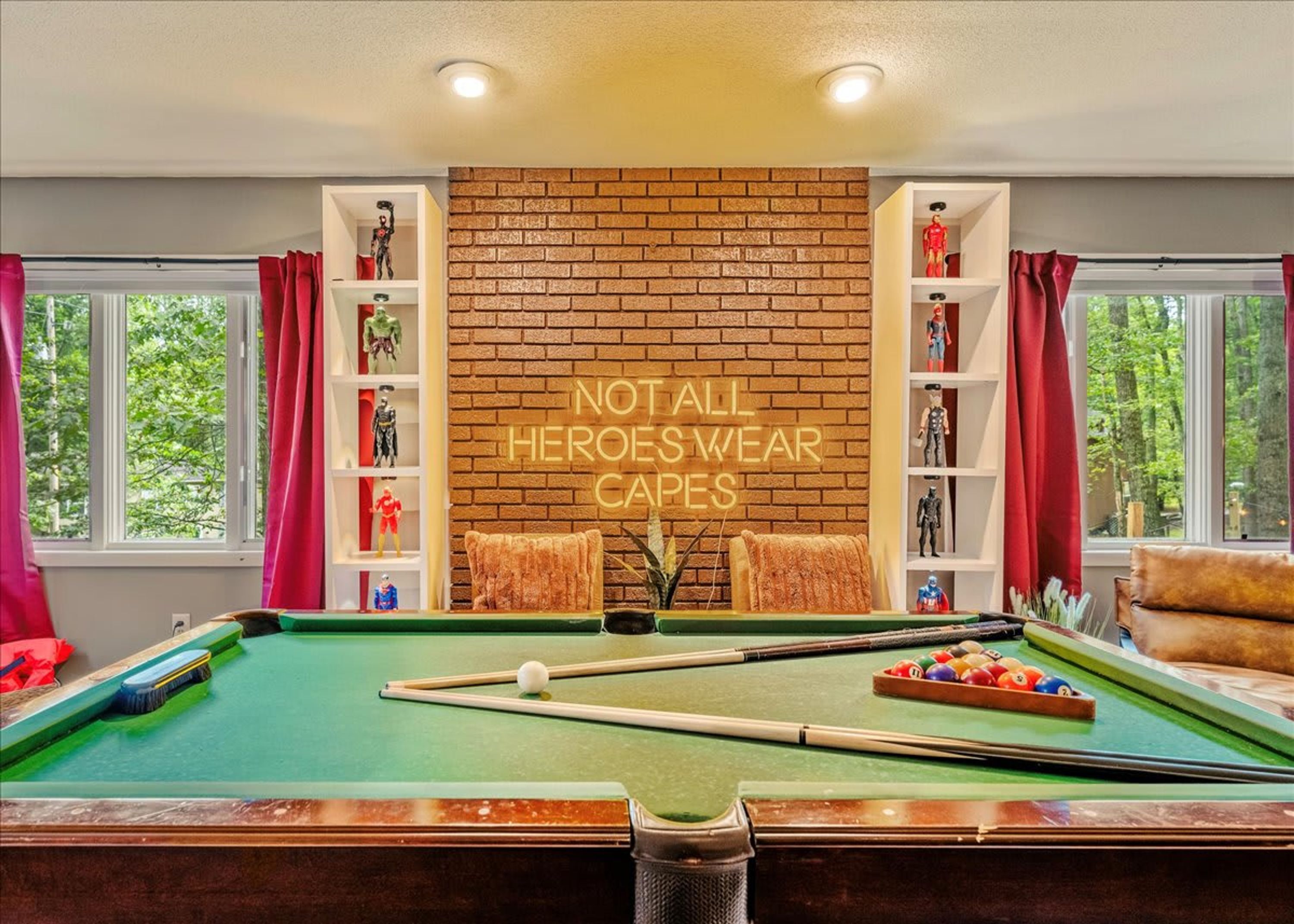 A pool table with a neon sign, a brick wall, and shelves with figurines.