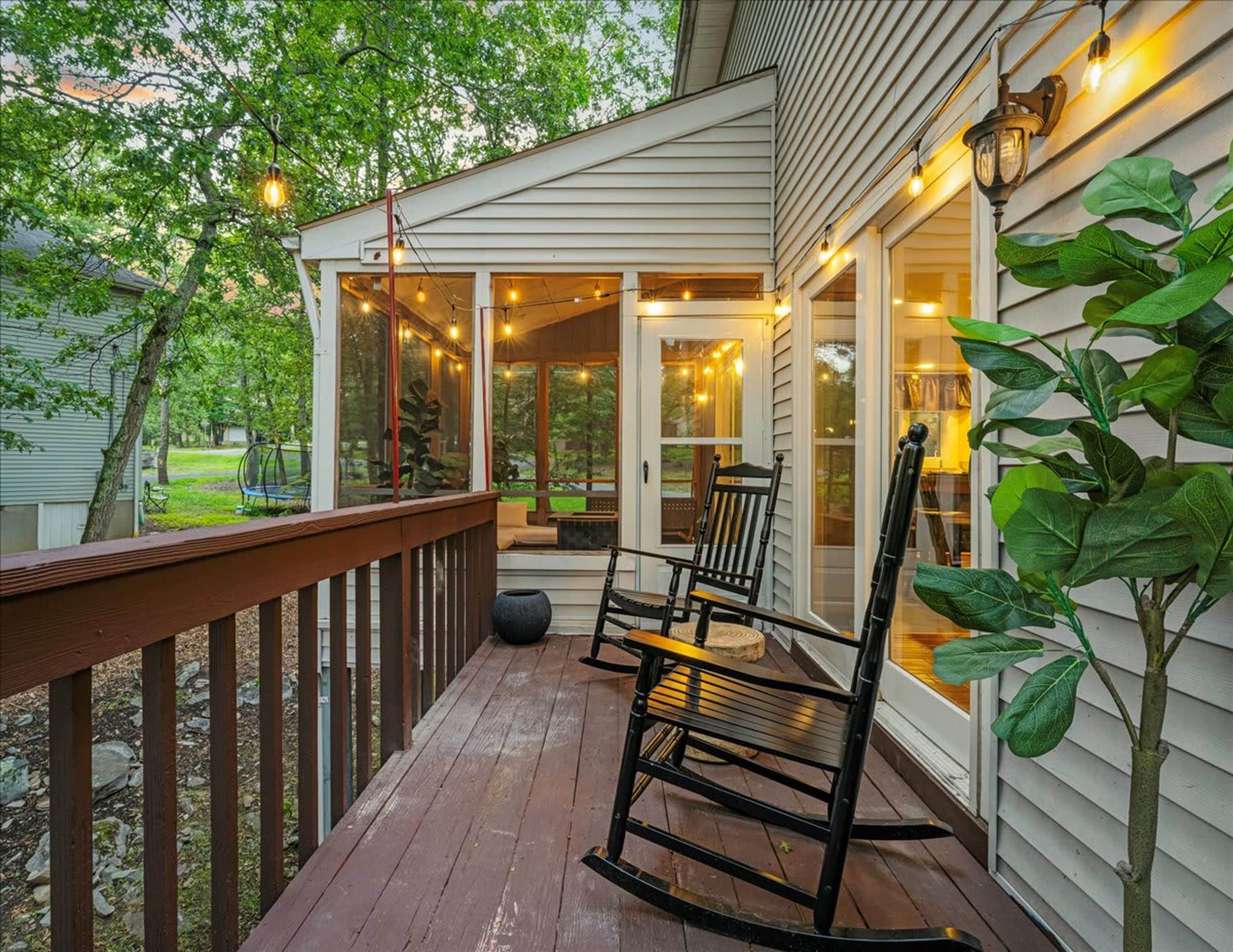A wooden deck with a rocking chair and a table, overlooking a garden.