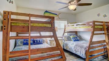 A room with two bunk beds, a ceiling fan, and a window with blinds.