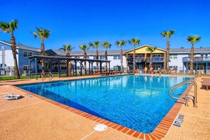 A swimming pool with a covered area, palm trees, and a clear blue sky. - Buena Vista- Ocean View Large Pool Boardwalk (Port Aransas)