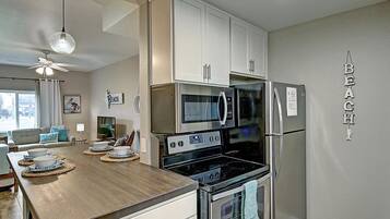 Eine moderne Küche mit weißen Schränken, einer Mikrowelle, einem Kühlschrank und einem Backofen. Ein Holztisch mit Schüsseln und einer Kaffeemaschine steht bereit.