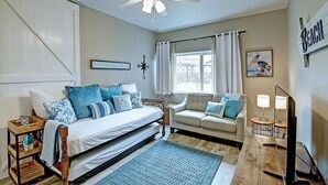 Quarto com cama, sofá, ventoinha no teto, janela com cortinas e placa fixada na parede.