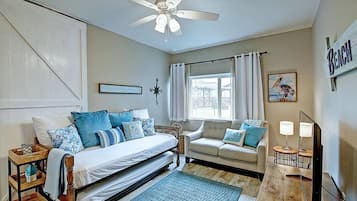A bedroom with a bed, a sofa, a ceiling fan, a window with curtains, and a wall-mounted sign.