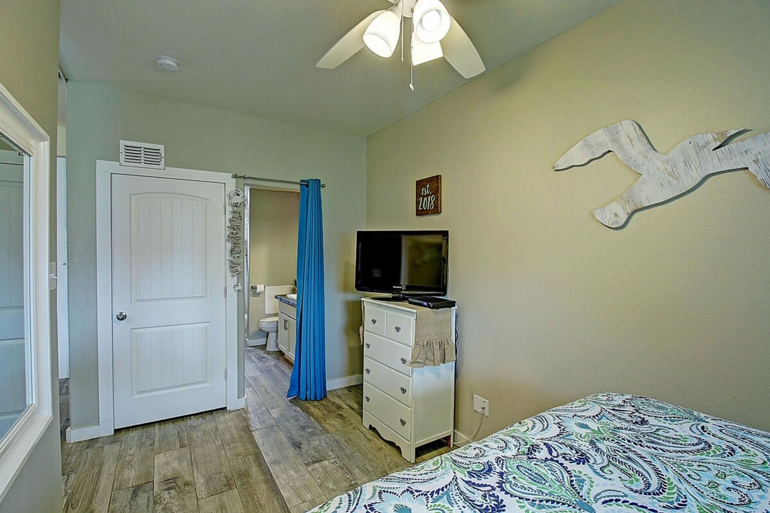 Un dormitorio con cama, cómoda, televisor y puerta que da al baño.