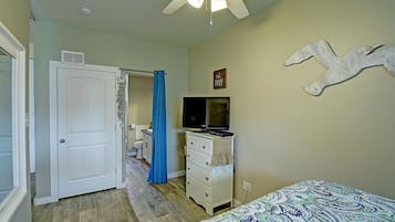Un dormitorio con cama, cómoda, televisor y puerta que da al baño.