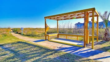 A wooden bench with a metal frame, located on a concrete path with grass on either side.