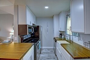 A compact kitchen with white cabinets, a stainless steel refrigerator, a microwave, and a stove. - Isle Getaway Boardwalk to Beach Community Pool (Port Aransas)