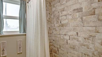 Un baño con pared de ladrillo, una ventana con cortinas y un interruptor de luz.