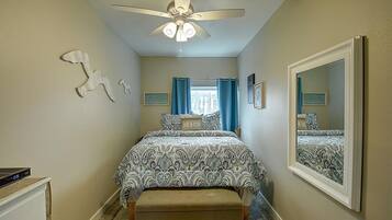 A bedroom with a bed, a ceiling fan, a dresser, a window with curtains, and a mirror.