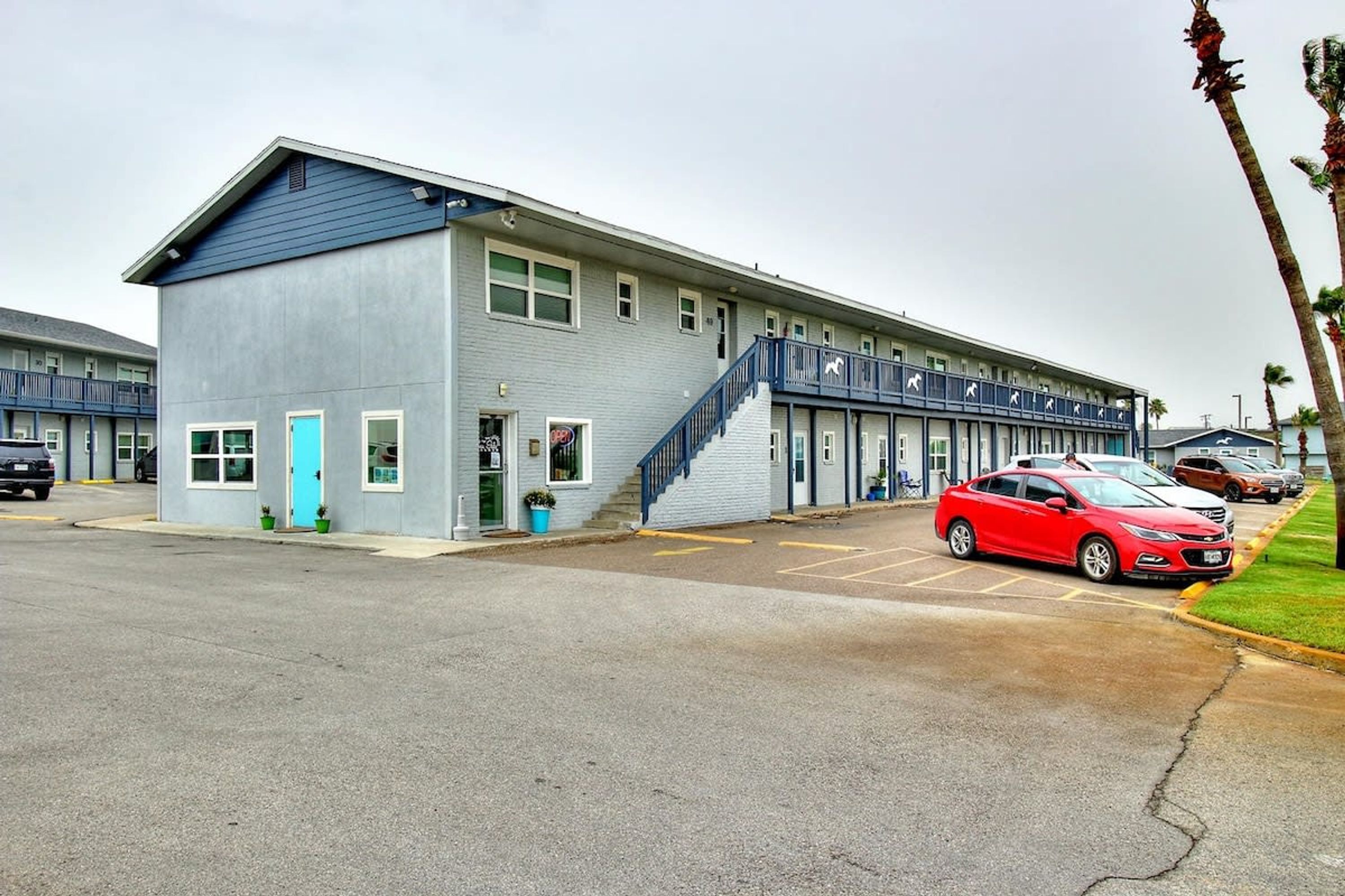 A motel with a two-story structure, a blue exterior, and a parking lot with several cars.