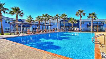 A swimming pool with lounge chairs and palm trees, surrounded by blue buildings.