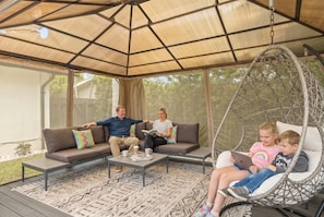 A covered outdoor seating area with a swing chair, a sofa, and a coffee table. - 2 Miles to Beach Pool Cabana Pool Table (Deerfield Beach)