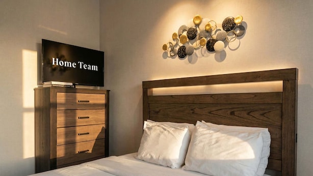 Um quarto com cama, cômoda, televisão e luminária na parede.