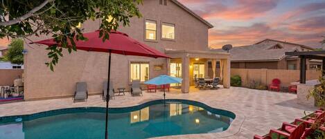 A residential property with a swimming pool, outdoor seating, and a two-story house.