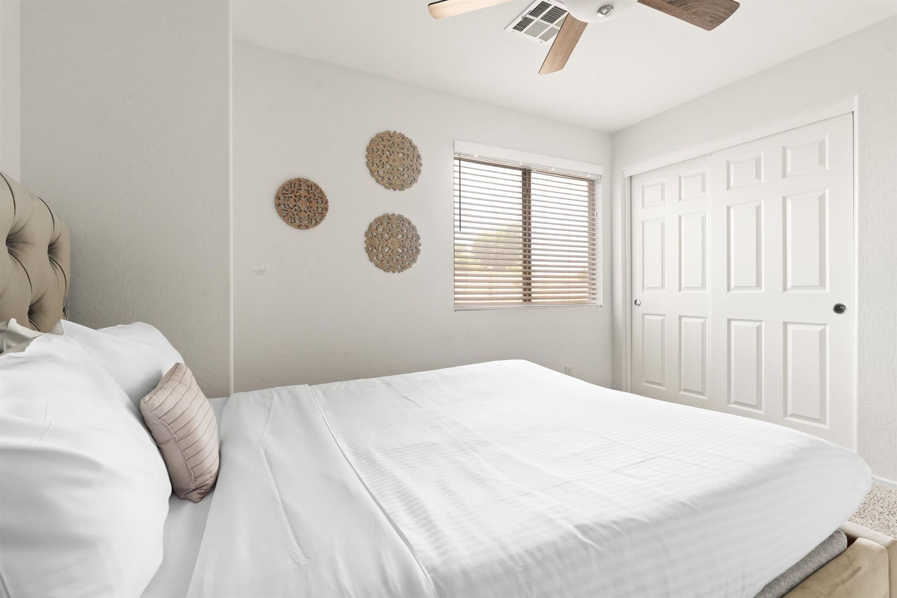 Une chambre à coucher avec un lit, un ventilateur de plafond, une fenêtre avec des stores et une porte.