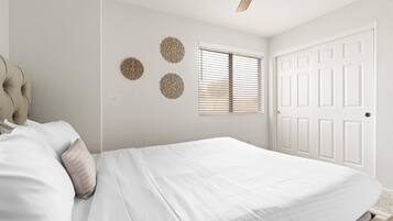Une chambre à coucher avec un lit, un ventilateur de plafond, une fenêtre avec des stores et une porte.