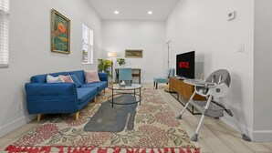 Uma sala de estar com um sofá azul, uma mesa de centro, uma televisão e um balanço para bebê.