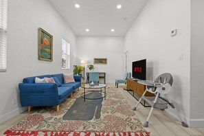 A living room with a blue sofa, a coffee table, a TV, and a baby rocker. - Pineapple Paradise 2 13 min to Beach Fire Pit (Sarasota)