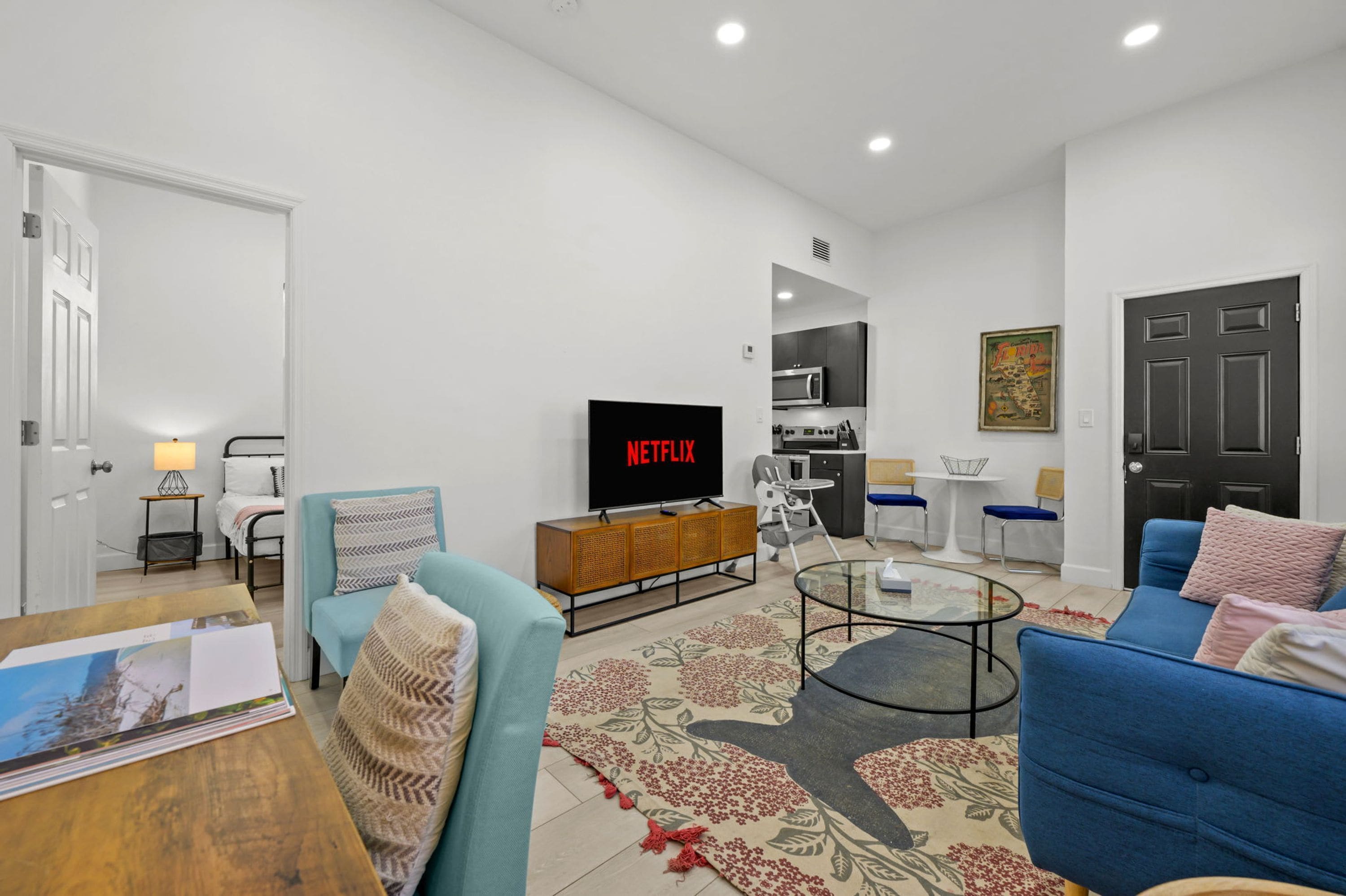 Una sala moderna con un televisor de pantalla plana, un sofá, una mesa de centro y una cocina al fondo.