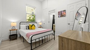 Um quarto com uma cama, abajures, uma janela, uma porta e um espelho.