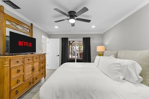 Habitació d'hotel amb un llit, una televisió que mostra 'NETFLIX', un ventilador de sostre i vista a l'exterior a través d'una porta.