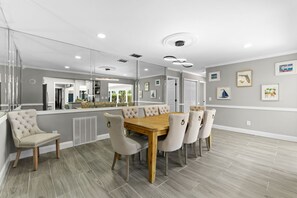 A dining area with a wooden table and upholstered chairs, a large mirror, and a view into the kitchen. - Sleeps 8 Tiki Bar Pool Hot Tub Fire Pit (Tampa)