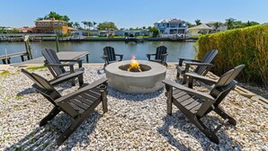 A waterfront outdoor seating area with a fire pit, surrounded by Adirondack chairs, overlooking a marina with boats and houses. - Sleeps 8 Tiki Bar Pool Hot Tub Fire Pit (Tampa)