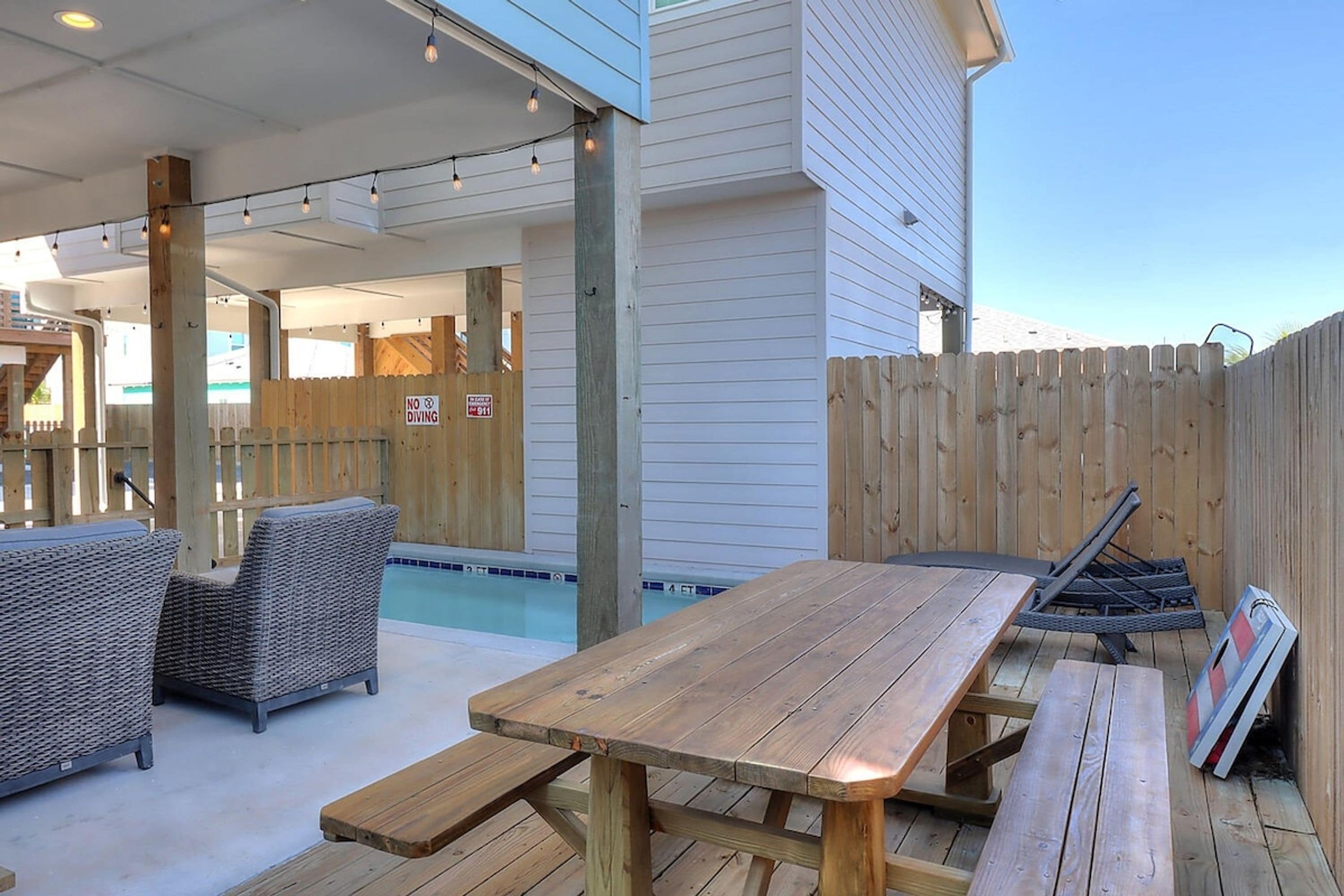 An outdoor patio area with a wooden table and chairs, a pool, and a wooden fence.