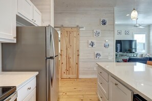 Una cuina moderna amb nevera d'acer inoxidable, terres de fusta i una porta corredissa que dona a una zona de menjador.