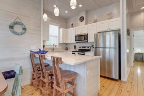 A modern kitchen with white cabinetry, stainless steel appliances, and a central island with bar stools. - Highway 9 Private Pool BBQ (Port Aransas)