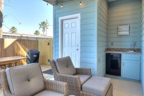A patio with wicker furniture, a barbecue grill, and a kitchen area with a refrigerator and sink. - Highway 9 Private Pool BBQ (Port Aransas)