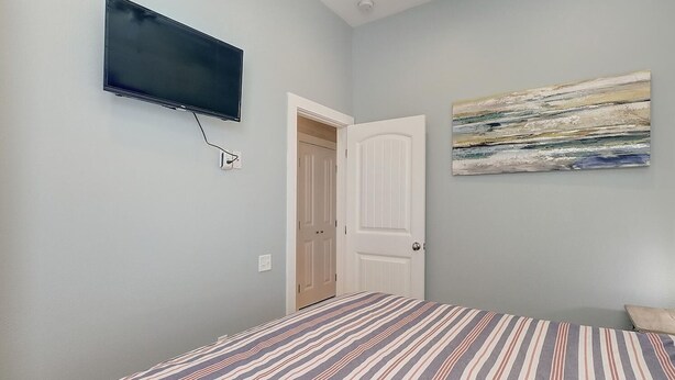 A bedroom with a bed, a television mounted on the wall, a door, and a painting. - Highway 9 Private Pool BBQ (Port Aransas)