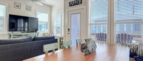 A spacious living room with a large wooden table, a television, and a sign indicating a beach direction.