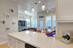 A modern kitchen with a large island, pendant lights, and a view of the beach through the windows. - Highway 9 Private Pool BBQ (Port Aransas)