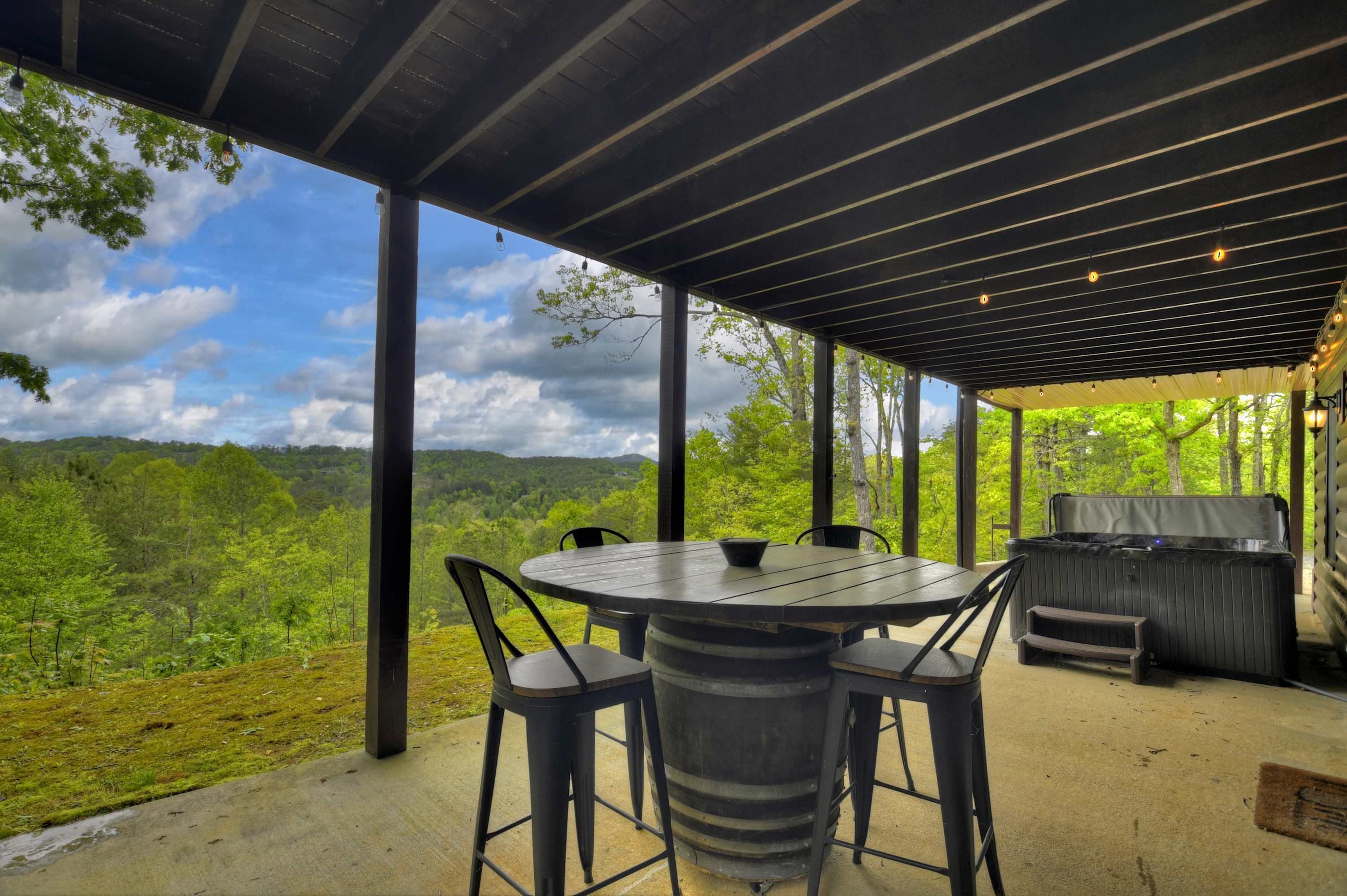 Un patio exterior con una mesa redonda y sillas, una parrilla y vistas a un paisaje boscoso.