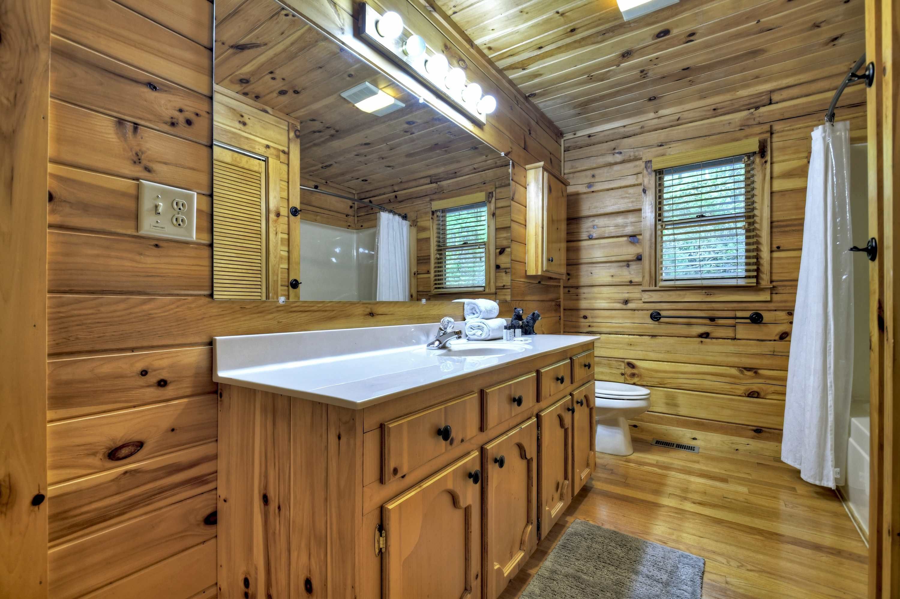 A wooden cabin bathroom with a large mirror, wooden cabinets, a sink, and a toilet.