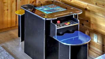 Una máquina recreativa pequeña y cerrada con un joystick y botones, ubicada en una cabaña de madera.