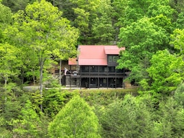 A two-story building with a red roof, surrounded by dense green forest.