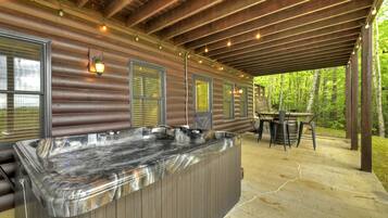 A covered outdoor area with a hot tub, wooden deck, and a table with chairs.