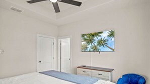 Un dormitorio con cama, ventilador de techo, televisor en la pared, escritorio y silla.