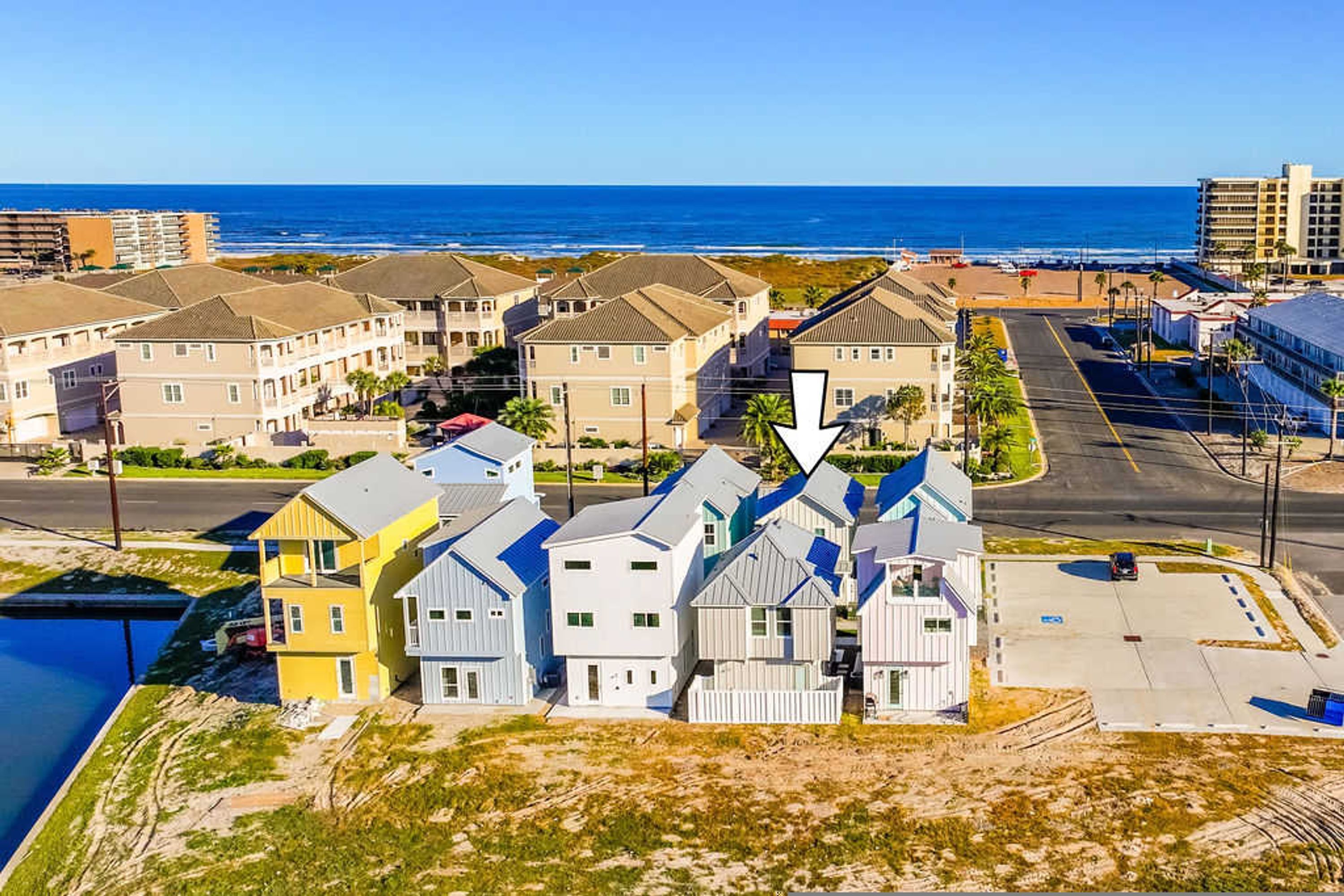 A coastal residential area with beachfront properties, a clear sky, and a view of the ocean.