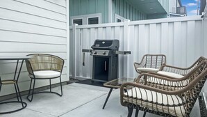 Un patio exterior con una parrilla, sillas de mimbre y una mesa.