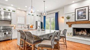 Uma cozinha moderna com eletrodomésticos de aço inoxidável, uma ilha central com banquetas e uma lareira.