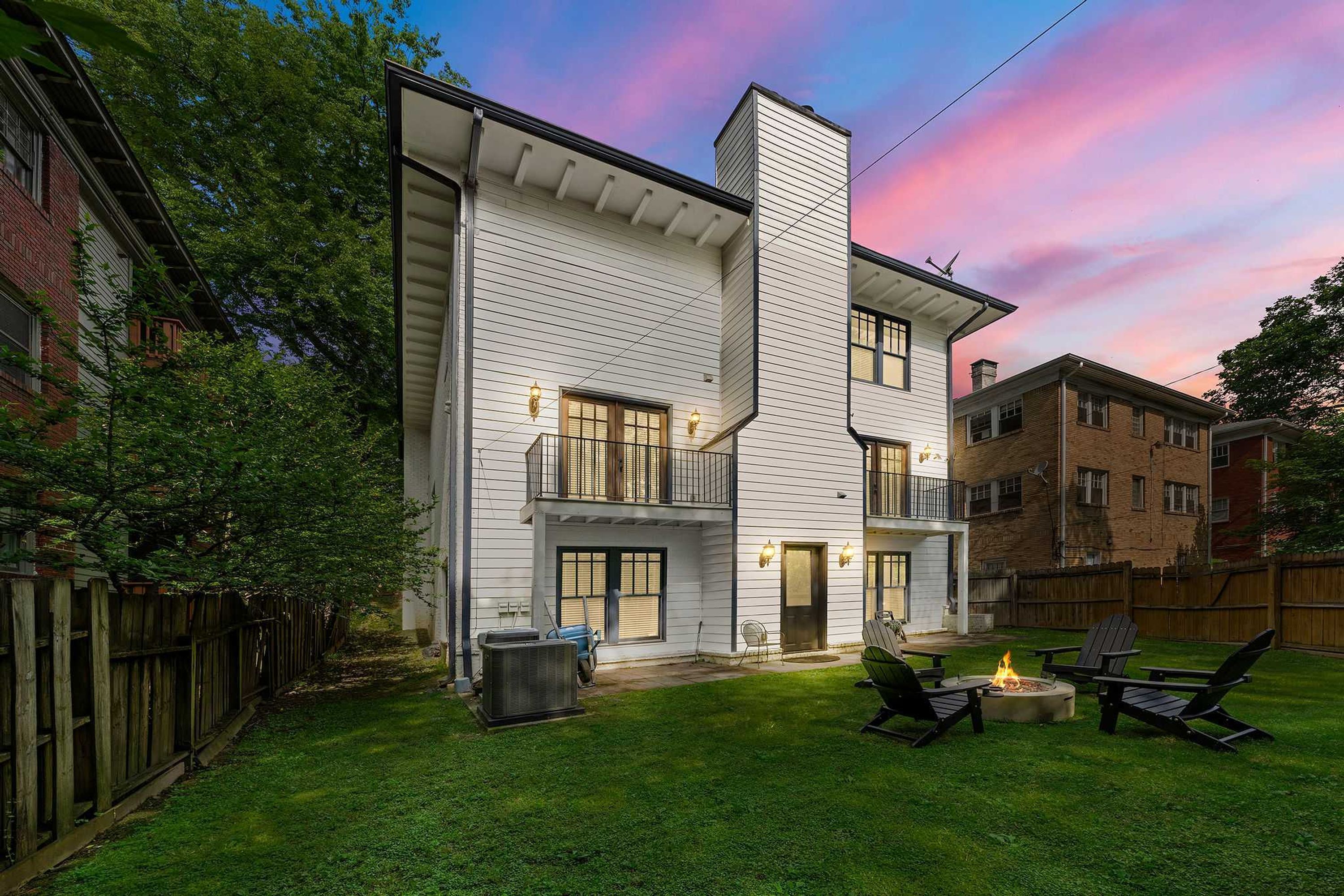 A two-story house with a white exterior, a visible chimney, and a backyard with a fire pit and outdoor seating.