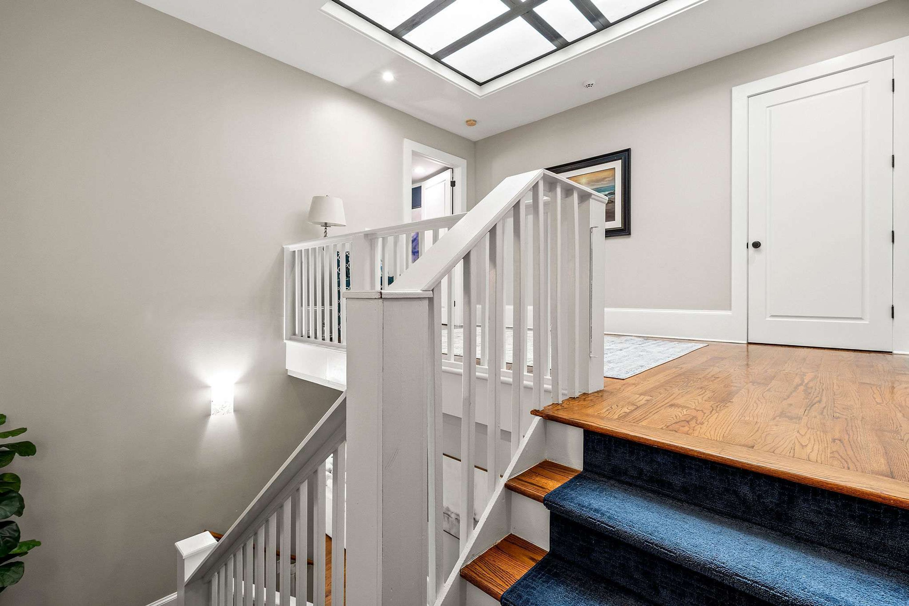 A staircase with white railings and wooden steps leading to a landing with a skylight.